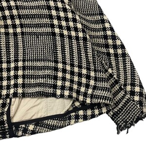 May include: Close-up of a black and white plaid jacket. The jacket has a classic houndstooth pattern. The interior lining is a light beige color. The edges of the jacket have a frayed, distressed look.