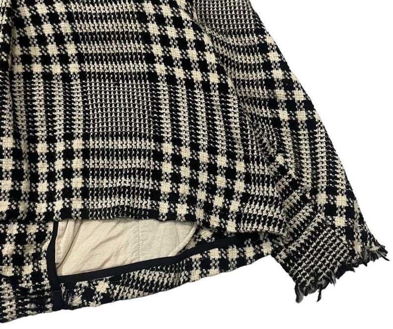 May include: Close-up of a black and white plaid jacket. The jacket has a classic houndstooth pattern. The interior lining is a light beige color. The edges of the jacket have a frayed, distressed look.