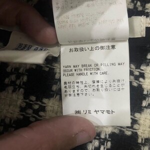 May include: Close-up of a white tag with Japanese text and English text. The English text reads: "YARN MAY BREAK OR PILLING MAY OCCUR WITH FRICTION. PLEASE HANDLE WITH CARE."