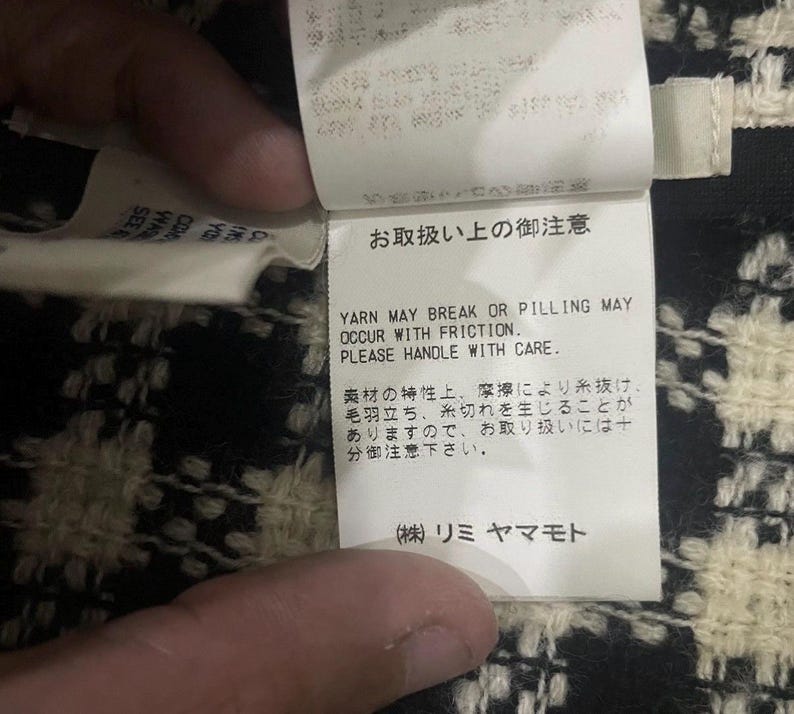 May include: Close-up of a white tag with Japanese text and English text. The English text reads: "YARN MAY BREAK OR PILLING MAY OCCUR WITH FRICTION. PLEASE HANDLE WITH CARE."