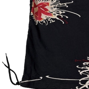 May include: Black garment with a floral design in red, cream, and white. The design features a large flower and flowing lines. The garment has a drawstring and the text "Evisu Dou" in red.