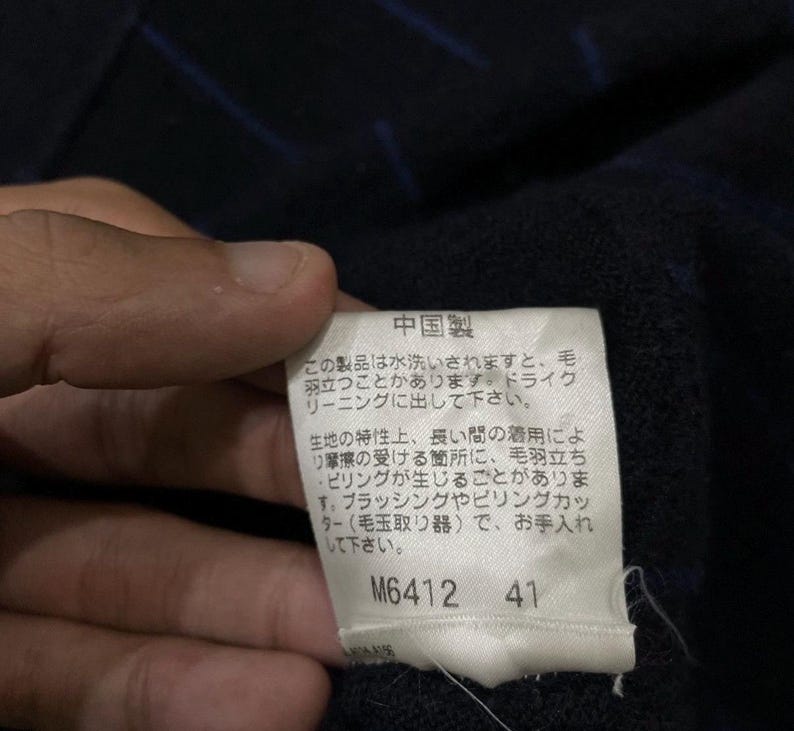 Puede incluir: Primer plano de una etiqueta con texto japon&eacute;s, adherida a una tela azul oscuro con rayas azules. La etiqueta es blanca con texto negro y los n&uacute;meros M6412 y 41.