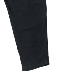 Puede incluir: Primer plano de un pantal&oacute;n negro. La tela es de color liso, con un ligero brillo. El dobladillo inferior es visible y el pantal&oacute;n est&aacute; ligeramente arrugado.