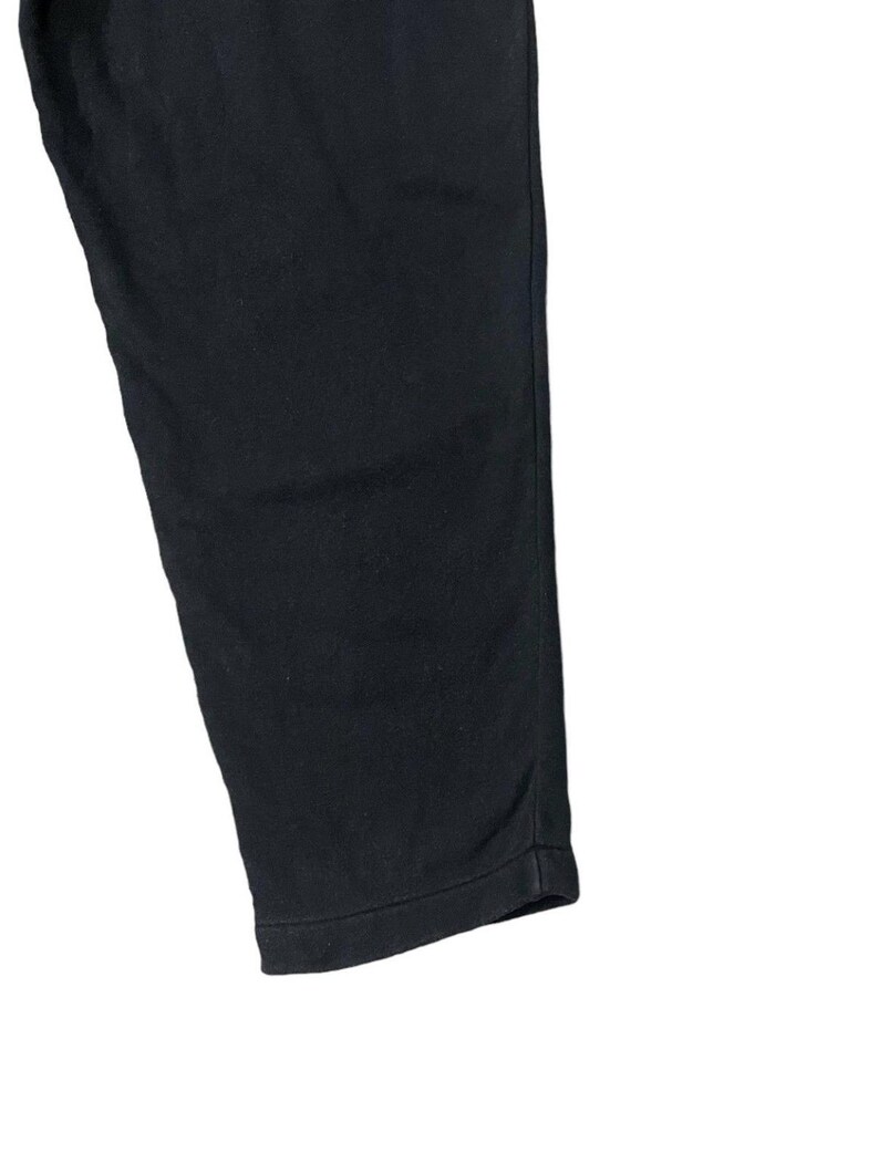Puede incluir: Primer plano de un pantal&oacute;n negro. La tela es de color liso, con un ligero brillo. El dobladillo inferior es visible y el pantal&oacute;n est&aacute; ligeramente arrugado.