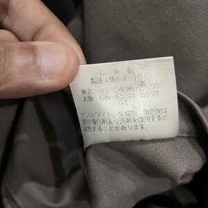 May include: Close-up of a tag with Japanese text and numbers. The tag is white with black text and is attached to a gray fabric. The text includes the words "Tokyo" and "Osaka" along with phone numbers.