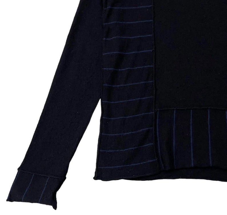 Puede incluir: Un su&eacute;ter de manga larga azul marino con un panel negro y detalles a rayas. La manga presenta un pu&ntilde;o acanalado con rayas a juego. El dise&ntilde;o del su&eacute;ter incluye patrones de rayas verticales y horizontales.