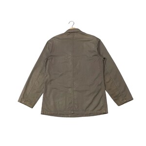 May include: A khaki-colored jacket with long sleeves and a button closure. The jacket is hanging on a hanger against a white background. The jacket has a simple, classic design.