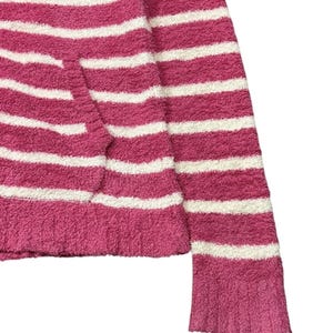May include: A close-up of a pink and white striped sweater. The sweater has a soft, fuzzy texture and a horizontal stripe pattern. The sleeve is visible, and the cuff has a ribbed design. The sweater is made of a thick, warm material.