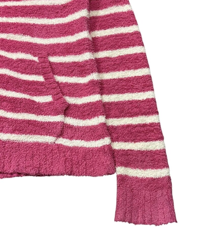 May include: A close-up of a pink and white striped sweater. The sweater has a soft, fuzzy texture and a horizontal stripe pattern. The sleeve is visible, and the cuff has a ribbed design. The sweater is made of a thick, warm material.