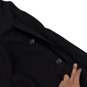 May include: Close-up of a black coat with two visible buttons and a pocket. The coat is made of a dark fabric and has a classic design. The buttons are round and black, and the pocket is rectangular.