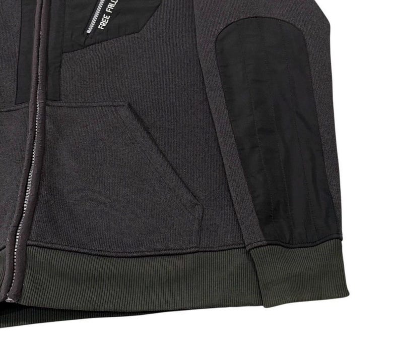 May include: A charcoal grey zip-up hoodie with black panels on the shoulders and chest. The hoodie features a ribbed hem and cuffs, a front pocket, and the text "FREE FALL" printed on the upper chest.