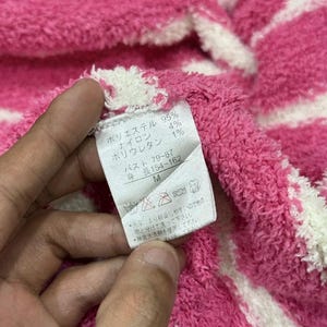 May include: Close-up of a pink and white striped fabric with a tag. The tag has Japanese text indicating the material composition and size. The fabric is soft and textured.