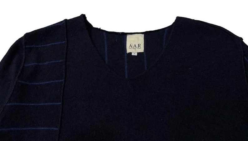 Puede incluir: Un su&eacute;ter azul marino con cuello en V con un dise&ntilde;o &uacute;nico. El hombro izquierdo presenta costuras azules horizontales, y l&iacute;neas azules verticales acent&uacute;an el frente. La etiqueta dice "A.A.R." en texto blanco.