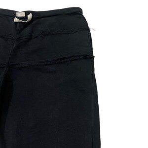 Puede incluir: Pantalones deportivos negros con cintura con cord&oacute;n y detalles desgastados. Los pantalones tienen un corte holgado y presentan costuras horizontales con bordes deshilachados, agregando una textura &uacute;nica. Un cord&oacute;n blanco es visible en la cintura.