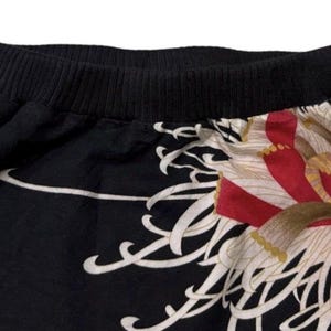 May include: Black skirt with a wide black waistband and a floral design. The skirt features a large, stylized flower in red, white, and gold. White, flowing lines accent the black fabric.