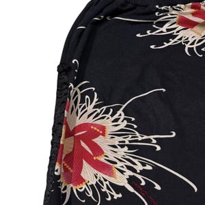 May include: Black fabric with a floral design of large red and white flowers. The design includes the text "Erica David" in a cursive font. The fabric has a gathered edge with black decorative accents.