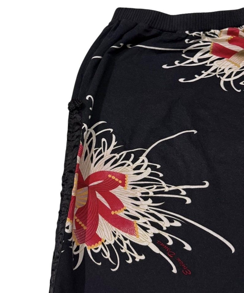 May include: Black fabric with a floral design of large red and white flowers. The design includes the text "Erica David" in a cursive font. The fabric has a gathered edge with black decorative accents.