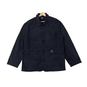 May include: A dark navy blue jacket with a collared neckline, button-down front, and two front pockets. The jacket has long sleeves and a small logo on the front pocket. The jacket is hanging on a wooden hanger.
