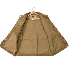 K&ouml;nnte beinhalten: Offene, hellbraune Cordjacke mit Knopfverschluss und zwei Vordertaschen. Sie h&auml;ngt an einem Holzkleiderb&uuml;gel. Das Innenfutter ist heller. Auf der Innenseite befindet sich ein Etikett.