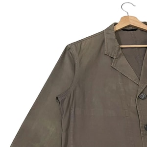 May include: A brown blazer with a notched lapel, two buttons, and a single-breasted design. The jacket is hanging on a wooden hanger against a white background. The blazer's fabric appears to be a solid color.