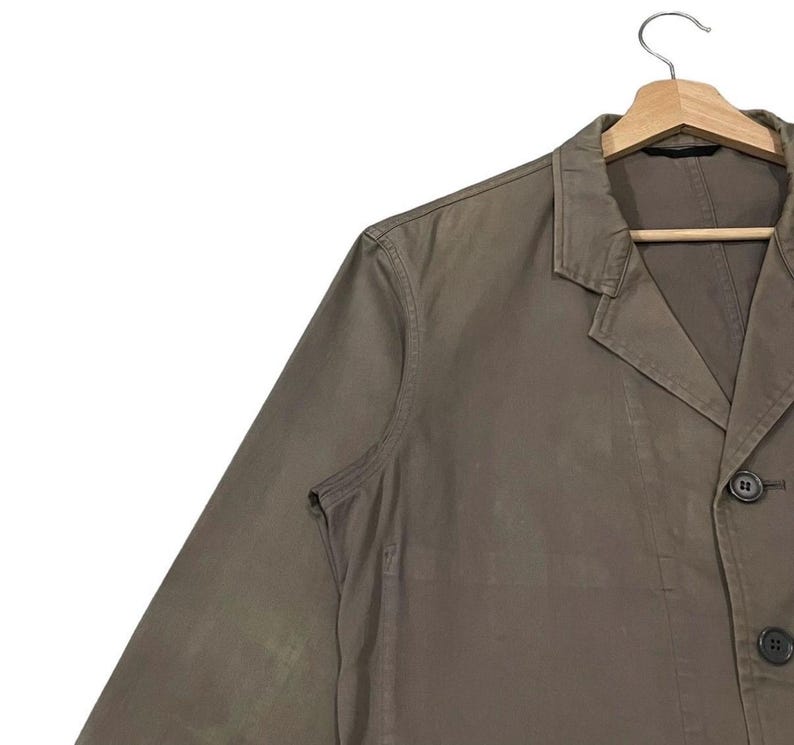 May include: A brown blazer with a notched lapel, two buttons, and a single-breasted design. The jacket is hanging on a wooden hanger against a white background. The blazer's fabric appears to be a solid color.