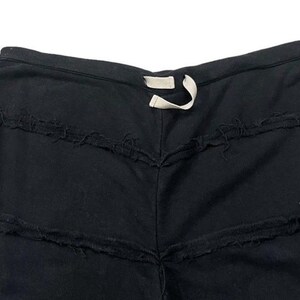 Puede incluir: Shorts negros con costuras horizontales deshilachadas y deshilachadas. Los pantalones cortos tienen una cintura con cord&oacute;n con un cord&oacute;n blanco. La prenda parece estar hecha de una tela oscura y suave.