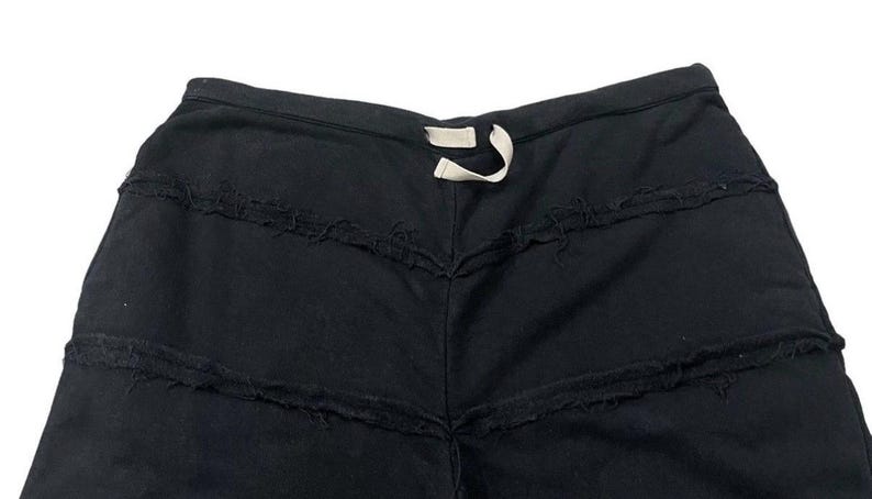 Puede incluir: Shorts negros con costuras horizontales deshilachadas y deshilachadas. Los pantalones cortos tienen una cintura con cord&oacute;n con un cord&oacute;n blanco. La prenda parece estar hecha de una tela oscura y suave.