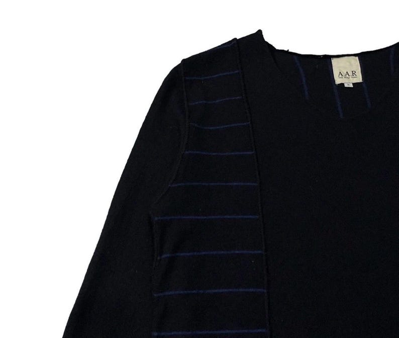 Puede incluir: Camiseta negra de manga larga con cuello redondo y un dise&ntilde;o &uacute;nico. La camiseta presenta rayas horizontales azul oscuro en la manga izquierda y un panel vertical. La etiqueta en la parte posterior del cuello dice "AAR".