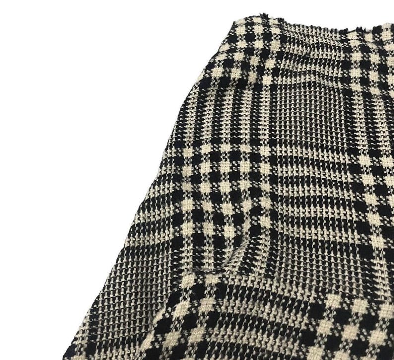 May include: Close-up of a black and white houndstooth pattern fabric. The fabric has a woven texture with a repeating pattern of small squares and vertical lines. The color scheme is a classic combination of black and off-white.