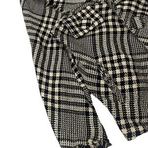 May include: Close-up of a black and white houndstooth patterned fabric. The fabric has a classic check design with a frayed edge. The material appears to be woven, with a textured surface. The overall look is a vintage or retro style.