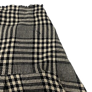 May include: Close-up of a black and white plaid skirt. The skirt has a classic pattern with a repeating grid design. The fabric appears to be a woven material. The skirt's hemline is visible, and the overall style is timeless.