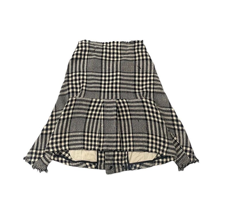 May include: A black, white, and gray plaid skirt. The skirt has a unique design with a pleated front and a flared shape. The fabric appears to be a woven material, and the hemline has a frayed edge. The skirt is displayed against a white background.
