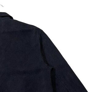 May include: A dark navy blue denim shirt with a button-down collar and long sleeves. The shirt is hanging on a white hanger against a white background. The fabric has a slightly textured appearance.