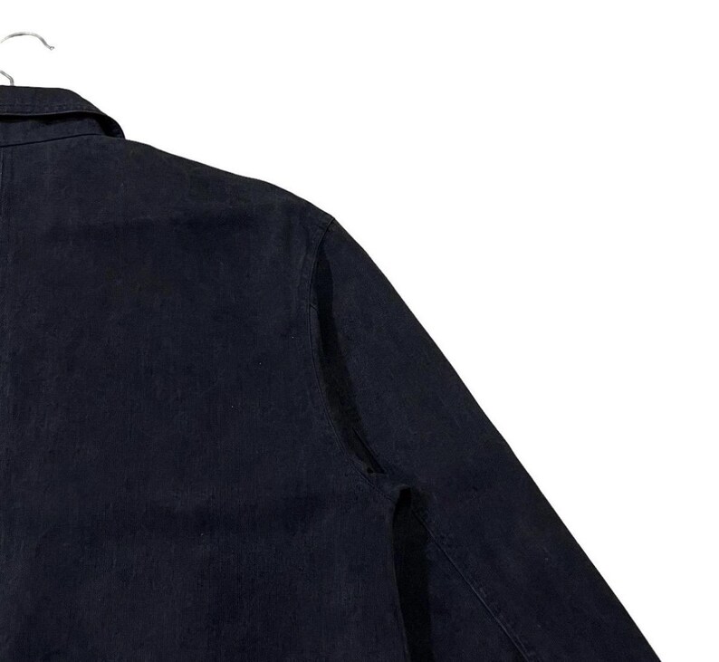 May include: A dark navy blue denim shirt with a button-down collar and long sleeves. The shirt is hanging on a white hanger against a white background. The fabric has a slightly textured appearance.