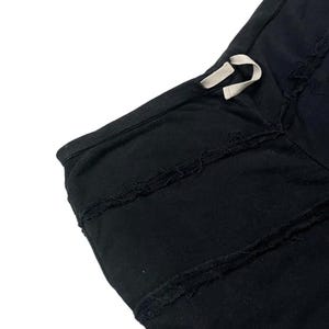 Puede incluir: Primer plano de tela negra con un dise&ntilde;o de bordes deshilachados. La prenda tiene un cord&oacute;n con un cord&oacute;n blanco. La tela parece ser un material suave, posiblemente algod&oacute;n o una mezcla de algod&oacute;n. El estilo general es informal.