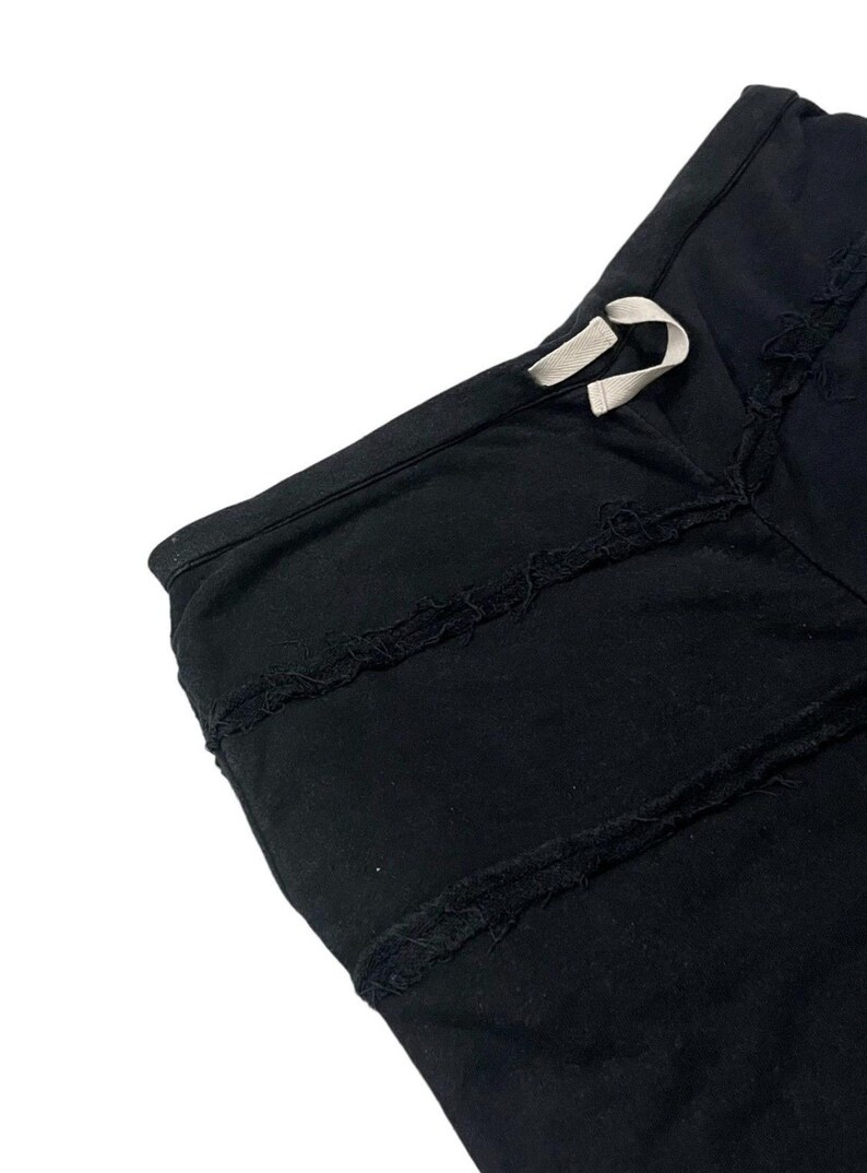 Puede incluir: Primer plano de tela negra con un dise&ntilde;o de bordes deshilachados. La prenda tiene un cord&oacute;n con un cord&oacute;n blanco. La tela parece ser un material suave, posiblemente algod&oacute;n o una mezcla de algod&oacute;n. El estilo general es informal.