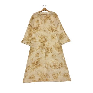 May include: A long-sleeved, knee-length dress in a light beige color featuring an all-over floral pattern in shades of tan and brown. The garment has a round neckline, a straight silhouette, and a visible zipper closure at the center back.