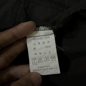 Puede incluir: Primer plano de una prenda negra con una etiqueta blanca. La etiqueta muestra texto japon&eacute;s, incluyendo "NO.2222-5380", "100% algod&oacute;n" y s&iacute;mbolos de cuidado. La tela parece ligeramente arrugada.