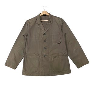 May include: A khaki-colored jacket with a button-up front, two large front pockets, and a single chest pocket. The jacket has long sleeves and a classic collar. The garment is hanging on a wooden hanger against a white background.