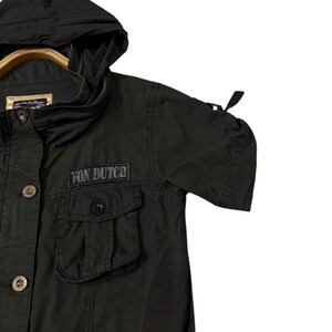 Puede incluir: Chaqueta negra con capucha con el texto "Von Dutch" en el pecho. La chaqueta tiene dos bolsillos delanteros, cierres de bot&oacute;n y una capucha con cord&oacute;n. Las mangas son cortas y tienen un detalle fruncido.
