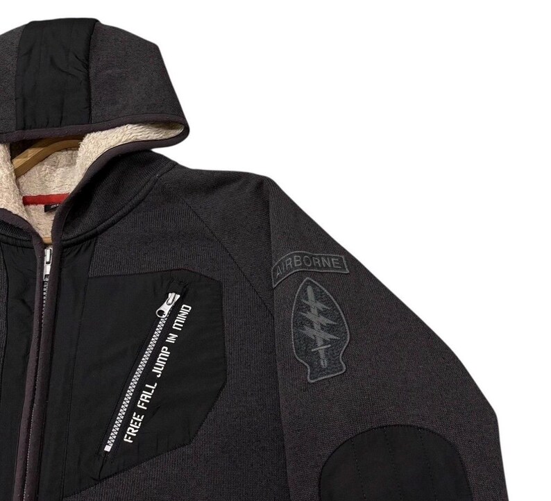 May include: Dark grey hooded jacket with a black chest panel and a black sleeve patch. The jacket features a zip closure and the text "FREE FALL JUMP IN MIND" is printed on the chest panel.