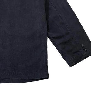 May include: A close-up shot of a navy blue jacket. The jacket features a buttoned cuff on the sleeve. The fabric looks to be a robust material, possibly denim or canvas. The jacket is a plain colour, with no visible patterns or designs.