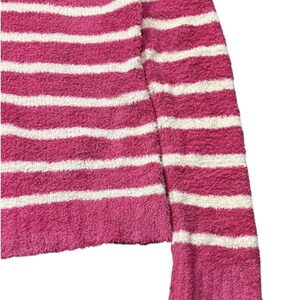 May include: A pink and white striped sweater with a soft, textured appearance. The sweater features horizontal stripes and a ribbed cuff on the sleeve. The fabric appears to be a plush material.