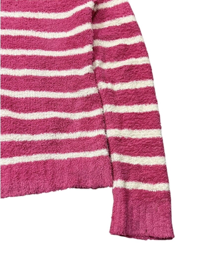 May include: A pink and white striped sweater with a soft, textured appearance. The sweater features horizontal stripes and a ribbed cuff on the sleeve. The fabric appears to be a plush material.