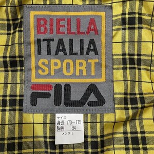 以下が含まれることがあります： 黄色と黒のチェック柄の生地のクローズアップ。ラベルには「BIELLA ITALIA SPORT」と赤、黒、黄色で書かれています。ブランド「FILA」も表示されています。ラベルはグレーで、黄色の縁取りがあります。