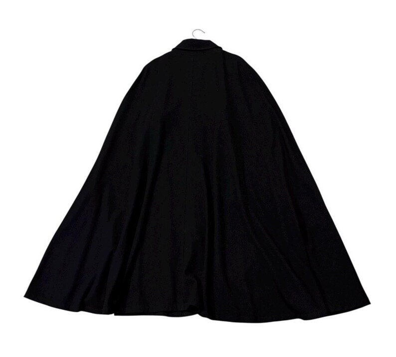 May include: A black cape with a buttoned collar, hanging from a hook. The cape is made of a dark fabric and has a wide, flowing design. The back view of the cape is shown, with the collar and shoulders visible.