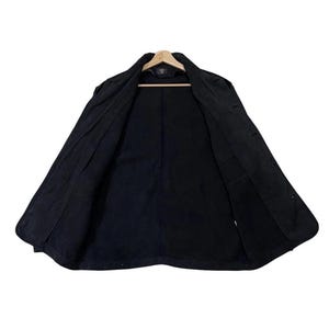 May include: A black jacket, open to show the interior, hanging on a wooden hanger. The jacket has a button-up front, a collar, and pockets. The lining is also black. The jacket appears to be made of a durable fabric.