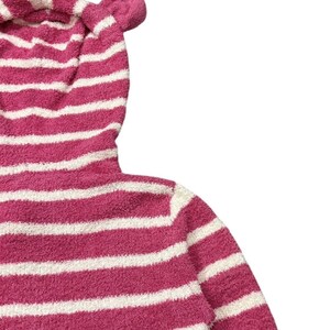 May include: A pink and white striped hooded sweatshirt with bear ears. The soft, plush fabric features horizontal stripes. The hood has two small, rounded ears at the top. The sweatshirt is a cozy, casual garment.
