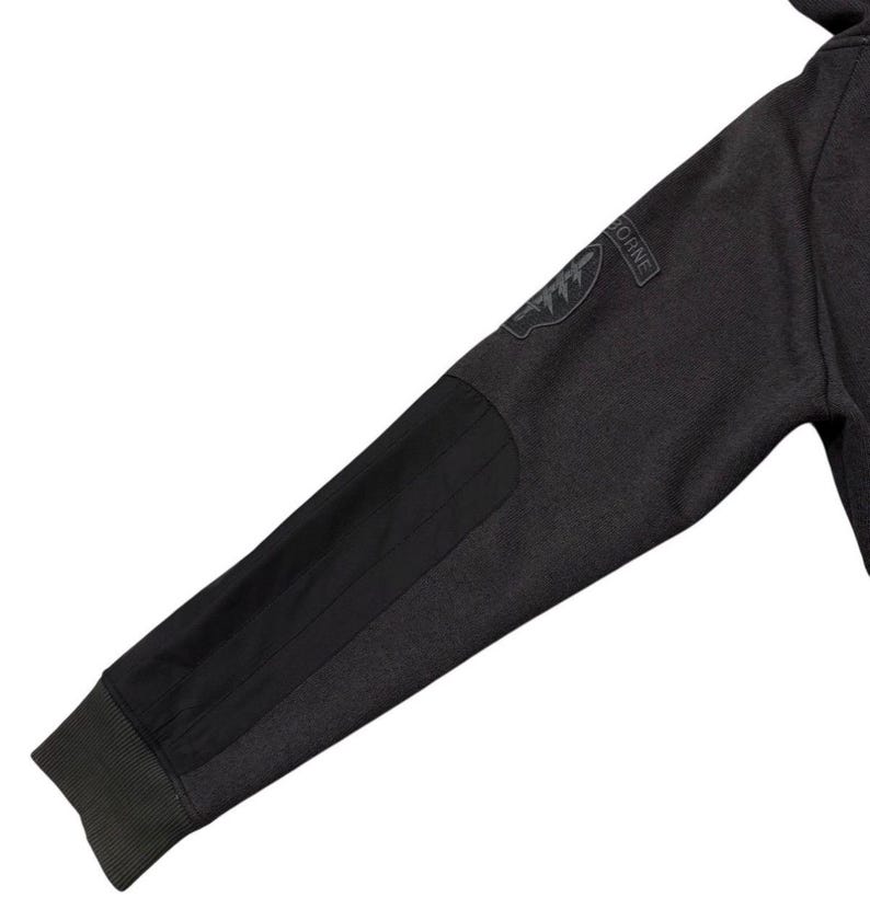 May include: Dark grey hoodie sleeve with a black elbow patch and a patch that says "AIRBORNE". The sleeve has a ribbed cuff and a black patch on the elbow.