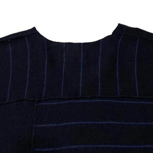 Puede incluir: Primer plano de una prenda azul marino con rayas azules verticales y horizontales. La tela parece ser un material texturizado, posiblemente lana. La prenda tiene un escote redondo.